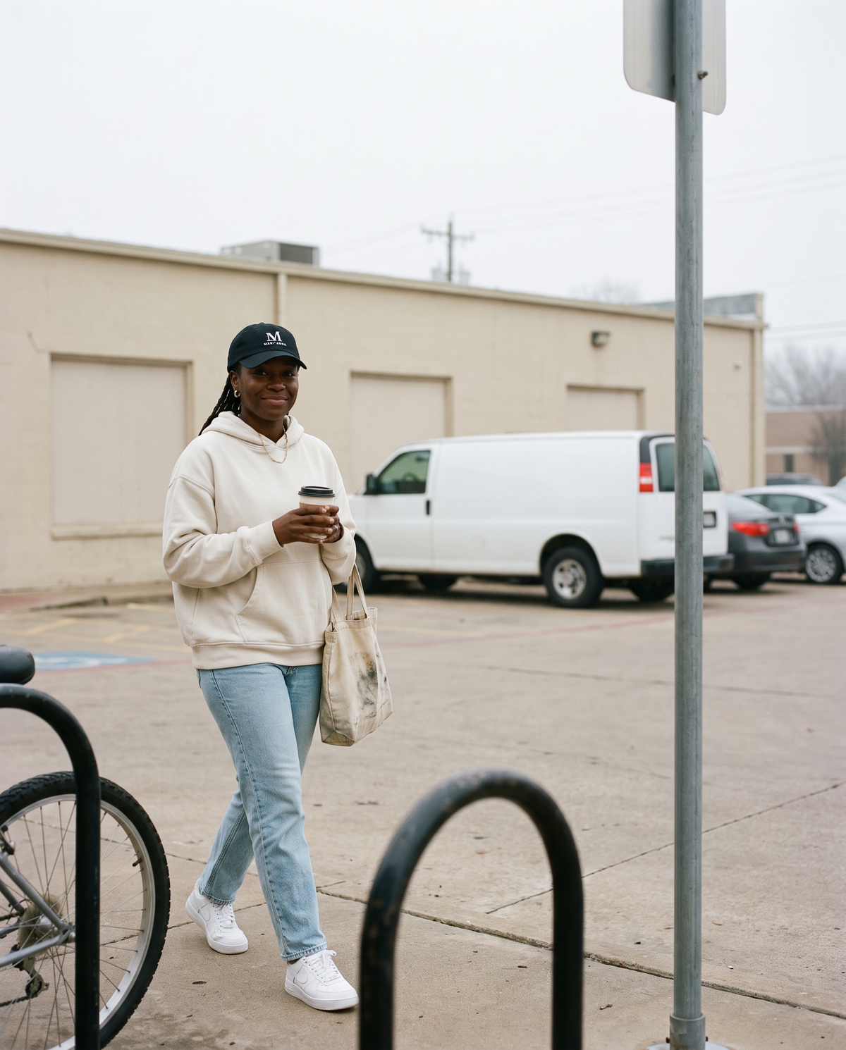 Woman in a bone hoodie walking down a city sidewalk wearing the black Mari'Anna dad cap