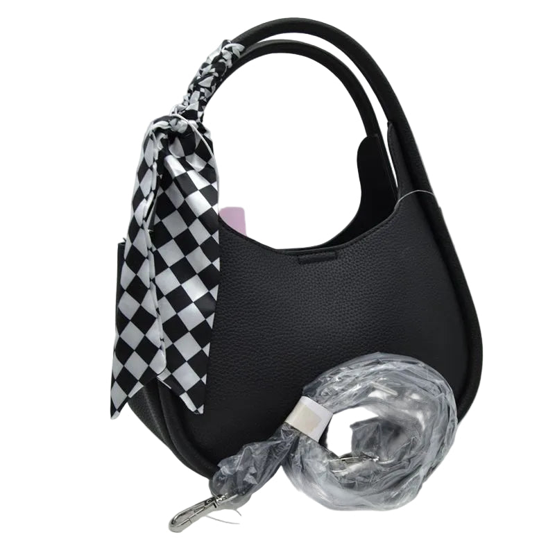 Black pebbled leather shoulder bag with a black and white checkered silk scarf tied to the handle, shown with its clear plastic-wrapped detachable shoulder strap on a white background.