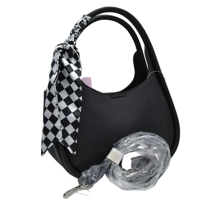 Black pebbled leather shoulder bag with a black and white checkered silk scarf tied to the handle, shown with its clear plastic-wrapped detachable shoulder strap on a white background.