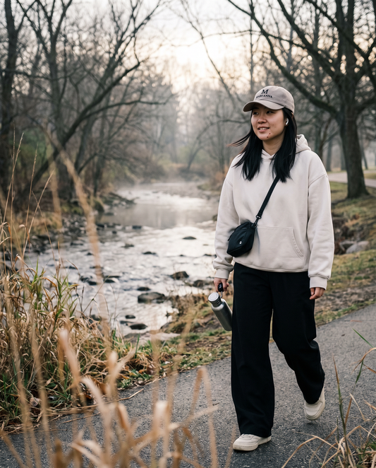 Woman in a bone hoodie walking a creek trail wearing the stone Mari'Anna dad cap