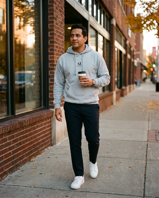 Man in a Carbon Grey Breakthrough M embroidered hoodie walking past a brick storefront with a coffee